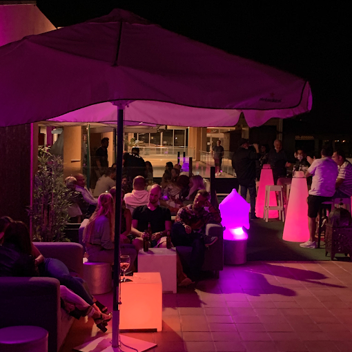 Terraza de DVN Lounge Club por la noche, con sombrillas e iluminación en tonos rosas
